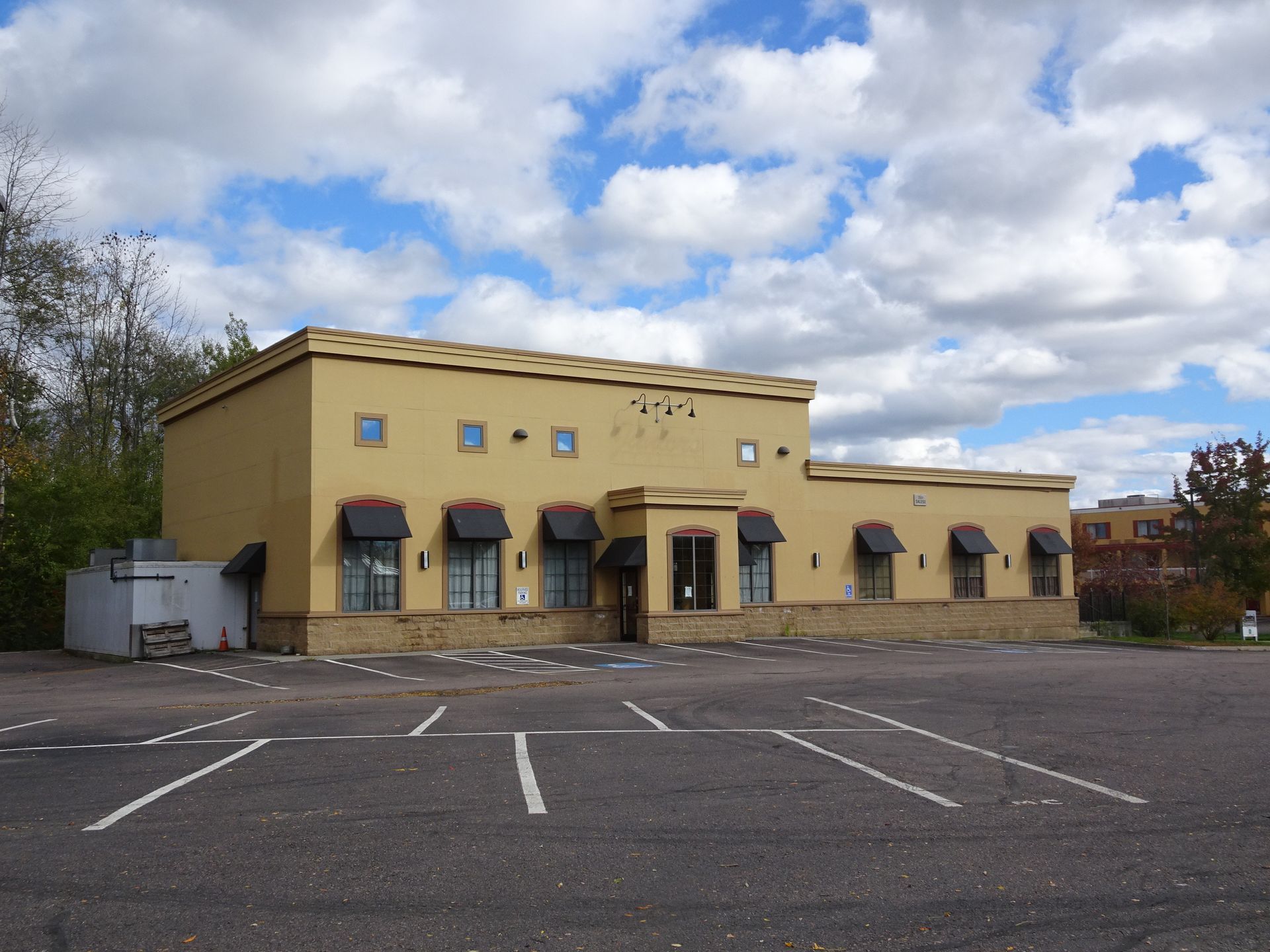 Yellow building with awnings and empty parking lot under a cloudy sky.
