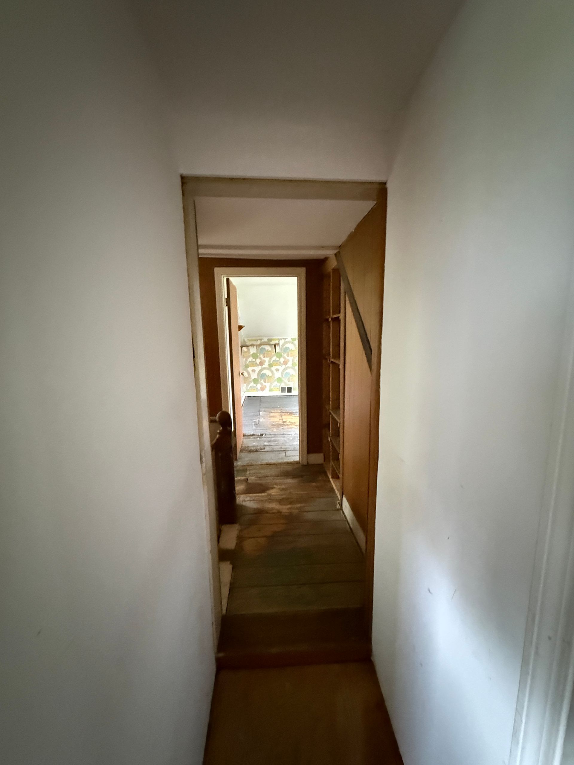 Narrow hallway with white walls leading to a doorway and stairwell beyond