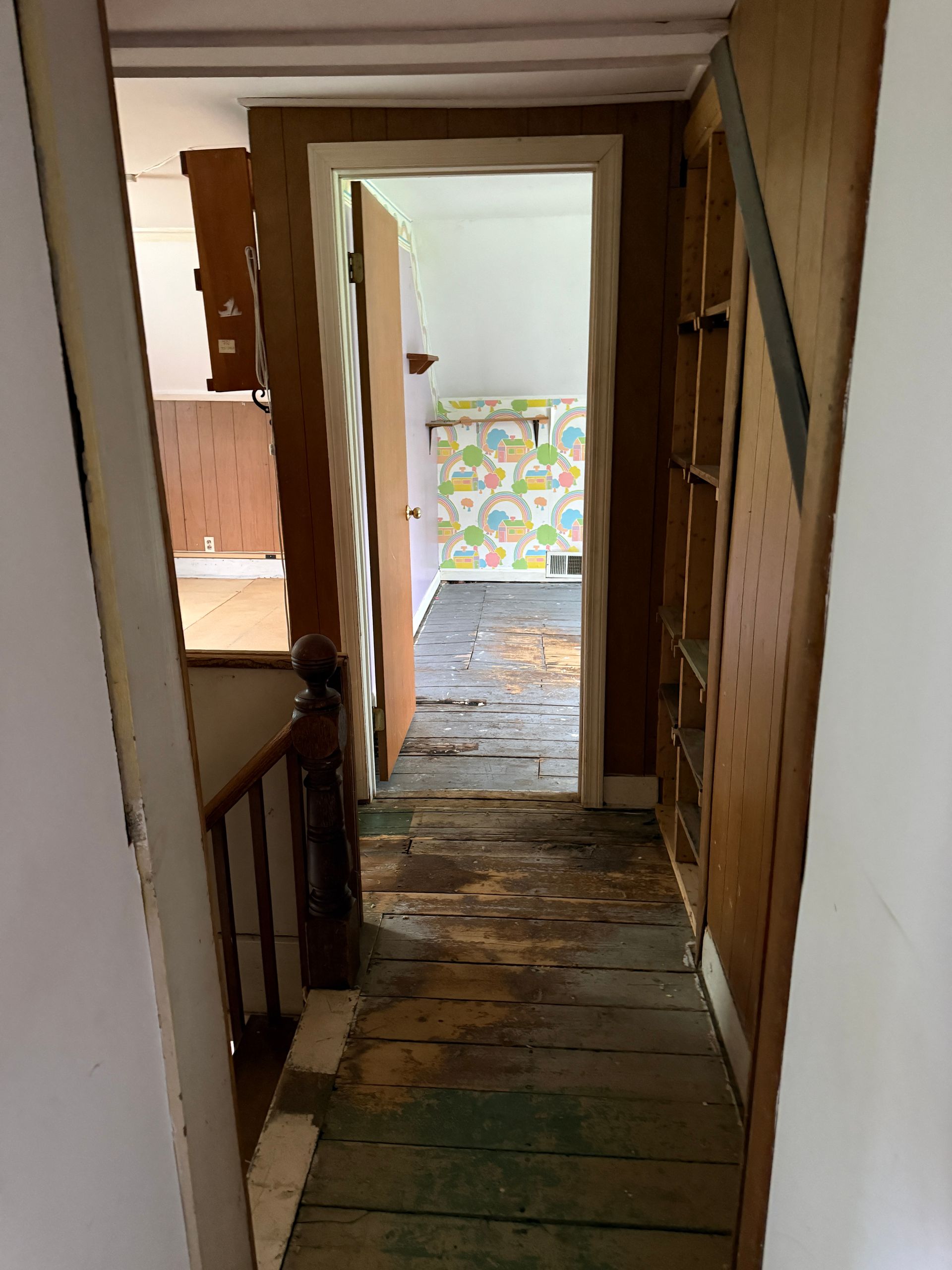 Narrow wooden hallway with floorboards leading to a bright doorway and colorful wall at the end