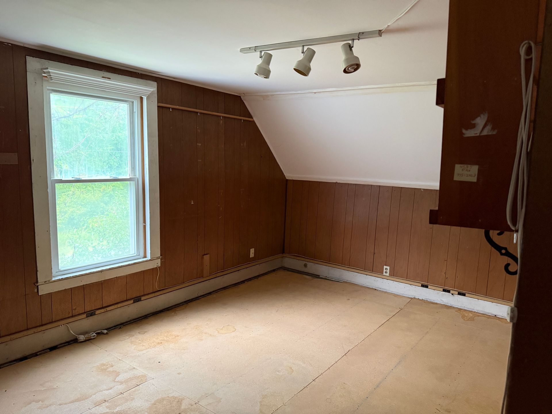 Empty wood-paneled room with a window, sloped ceiling, and track lighting