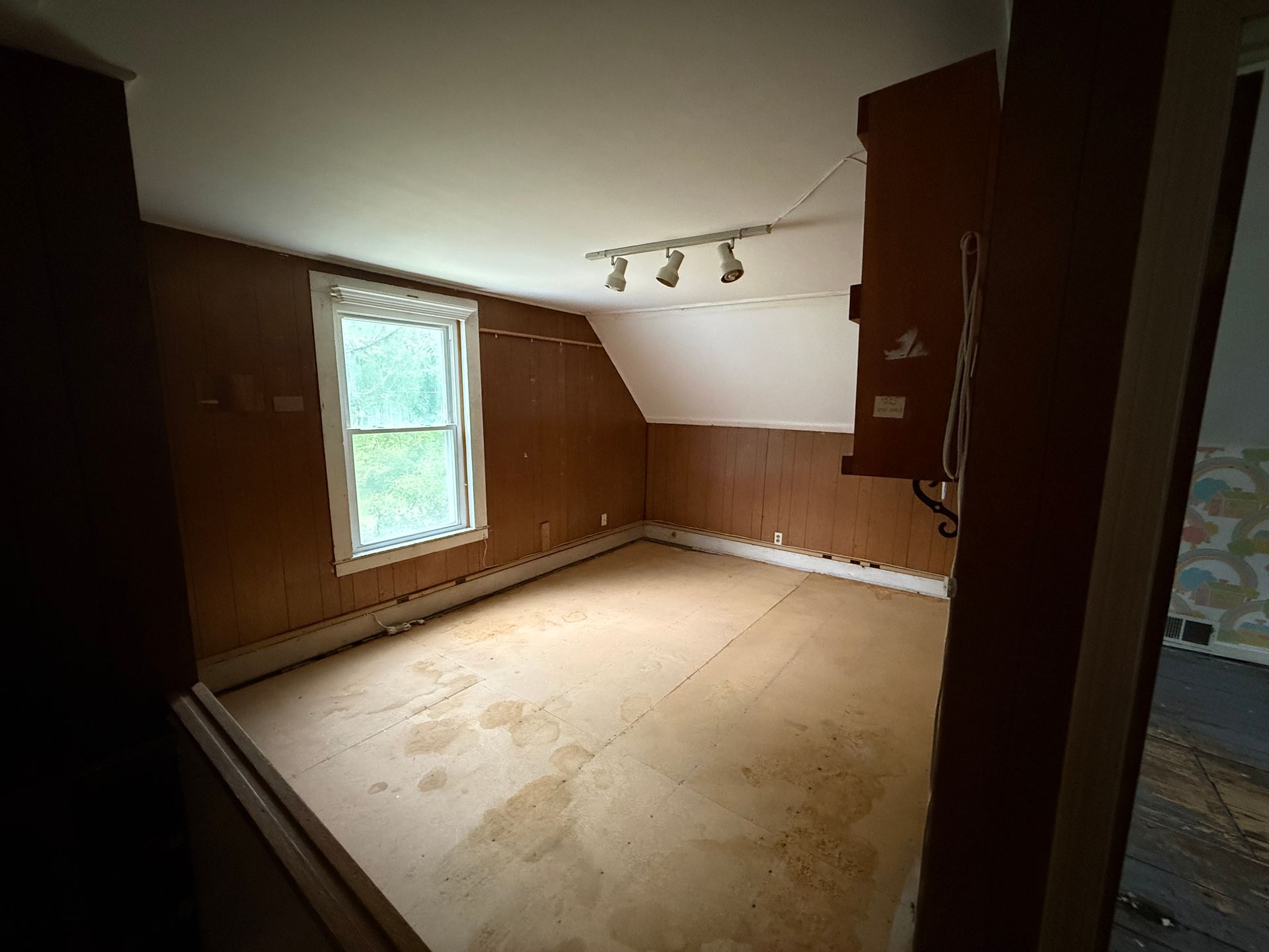 Empty wood-paneled room with a window and track lights