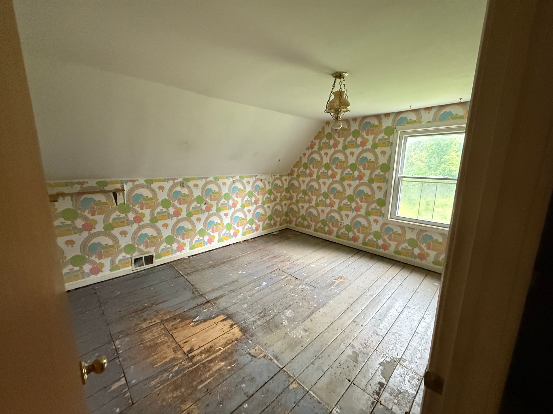 Empty room with floral wallpaper, wooden floor, and a window on the right.