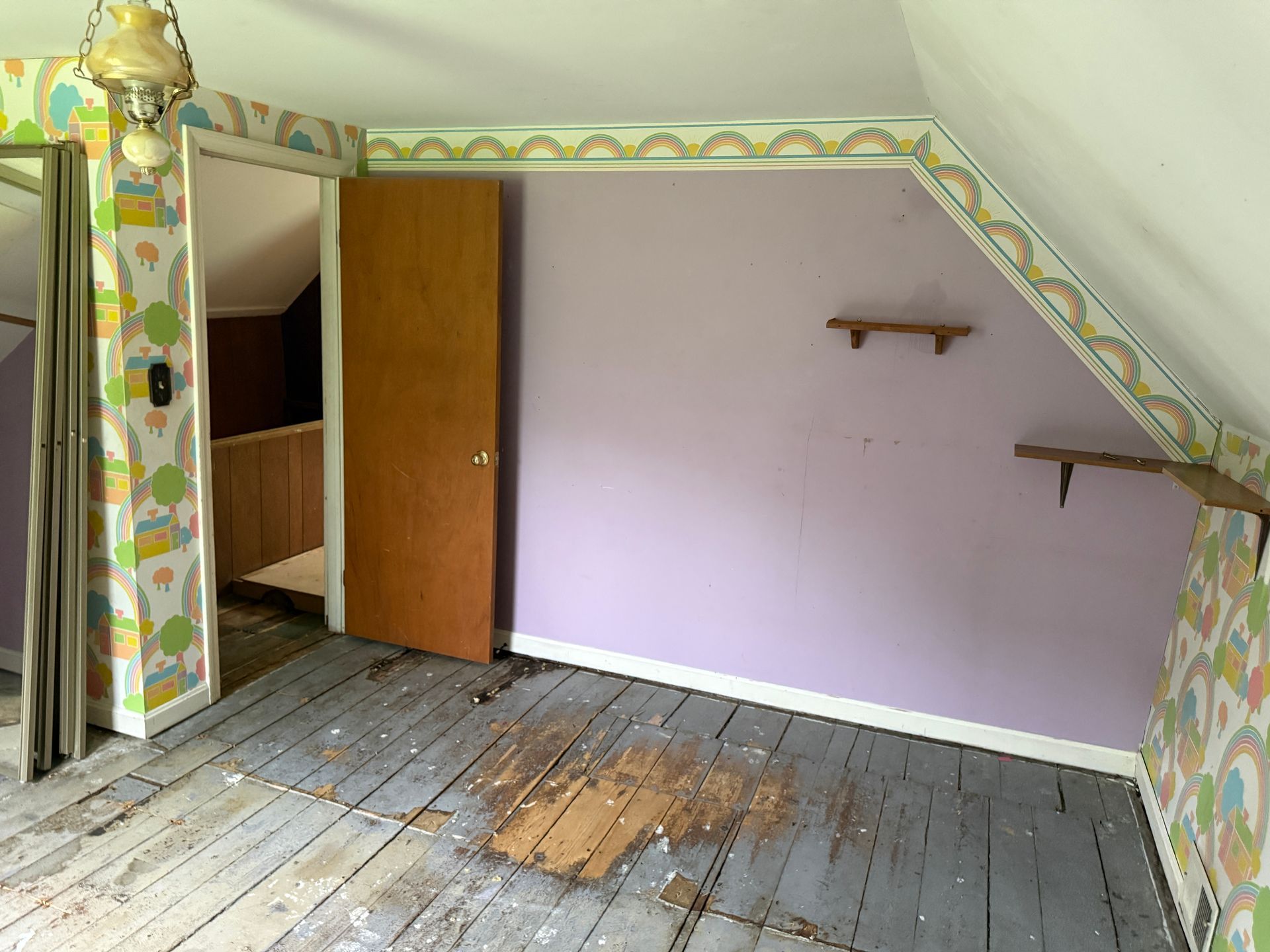 Empty attic room with slanted ceiling, worn wooden floor, purple wall, and open closet door