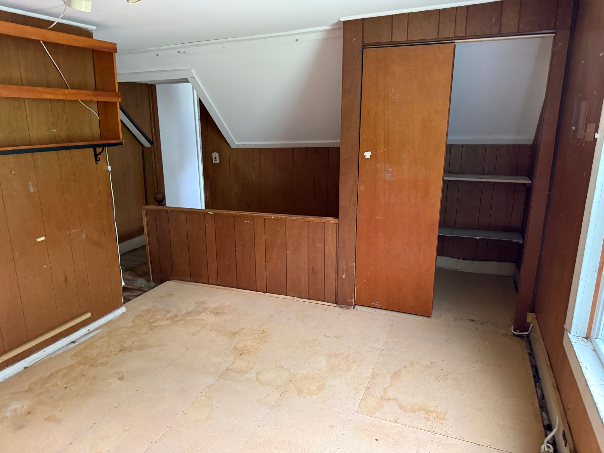 Empty carpeted room with wood-paneled walls, built-in shelves, and open closet doors.