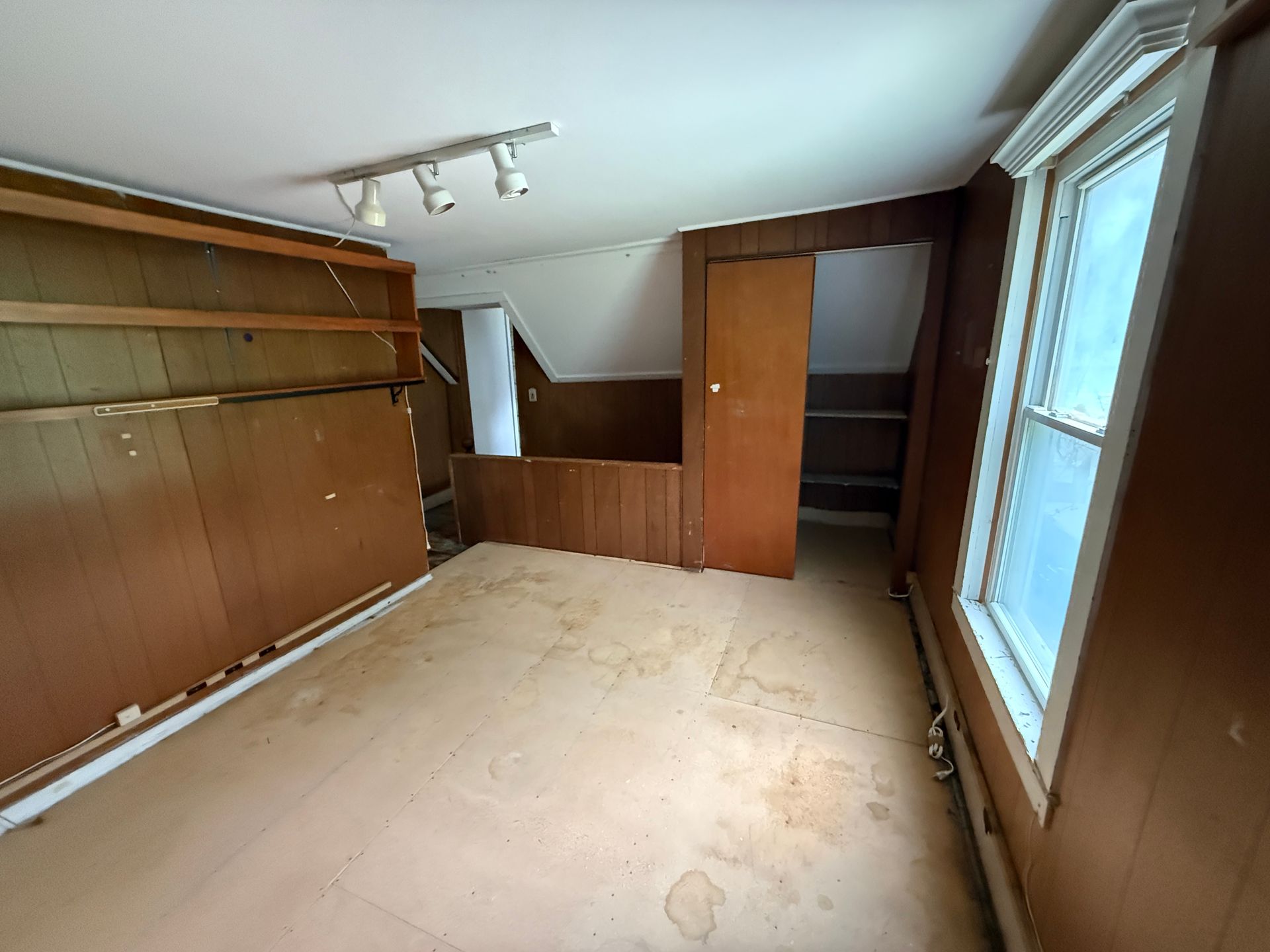 Empty wood-paneled room with built-in shelving and large windows along one wall