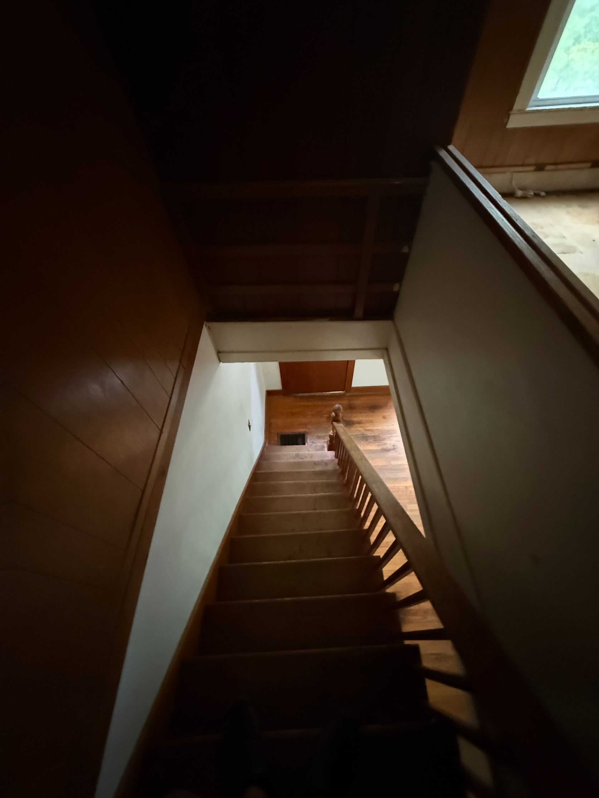stairwell with wooden steps, white walls, and sunlight from a window at the top.