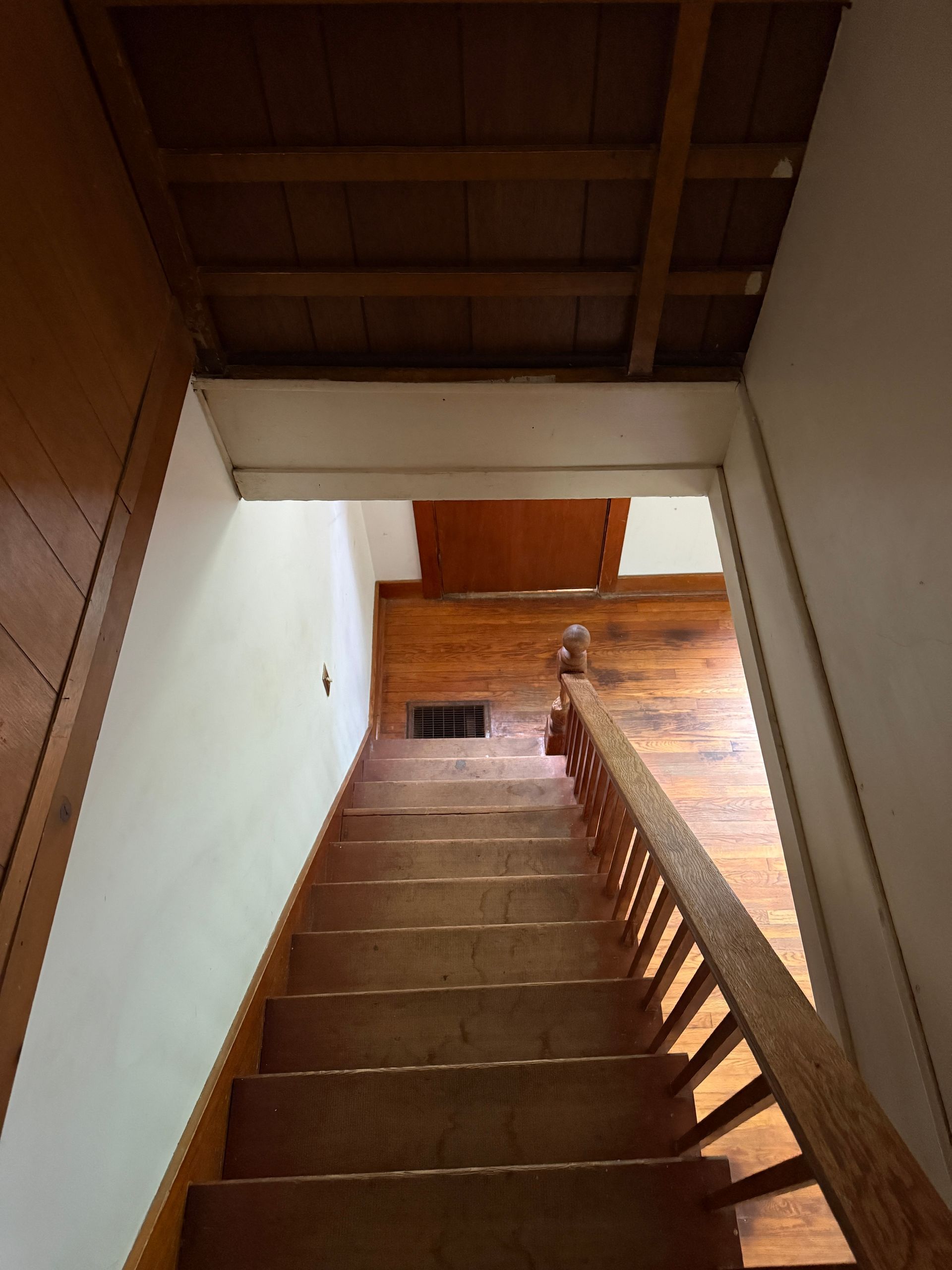 Steep wooden staircase descending to a lower floor with white walls and a wood handrail
