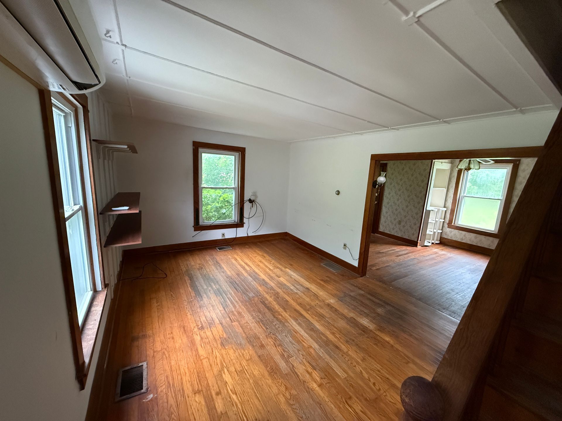 Empty room with hardwood floors, white walls, two windows, and an open doorway to another room.