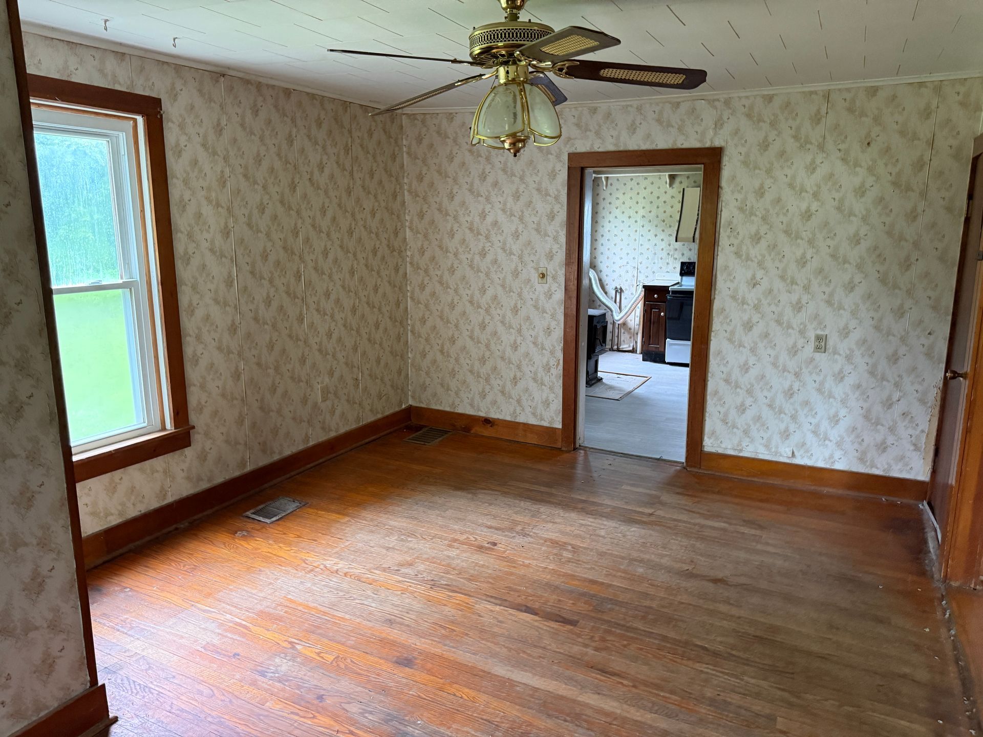 Empty room with wood floors, patterned wallpaper, ceiling fan, and a doorway to another room.