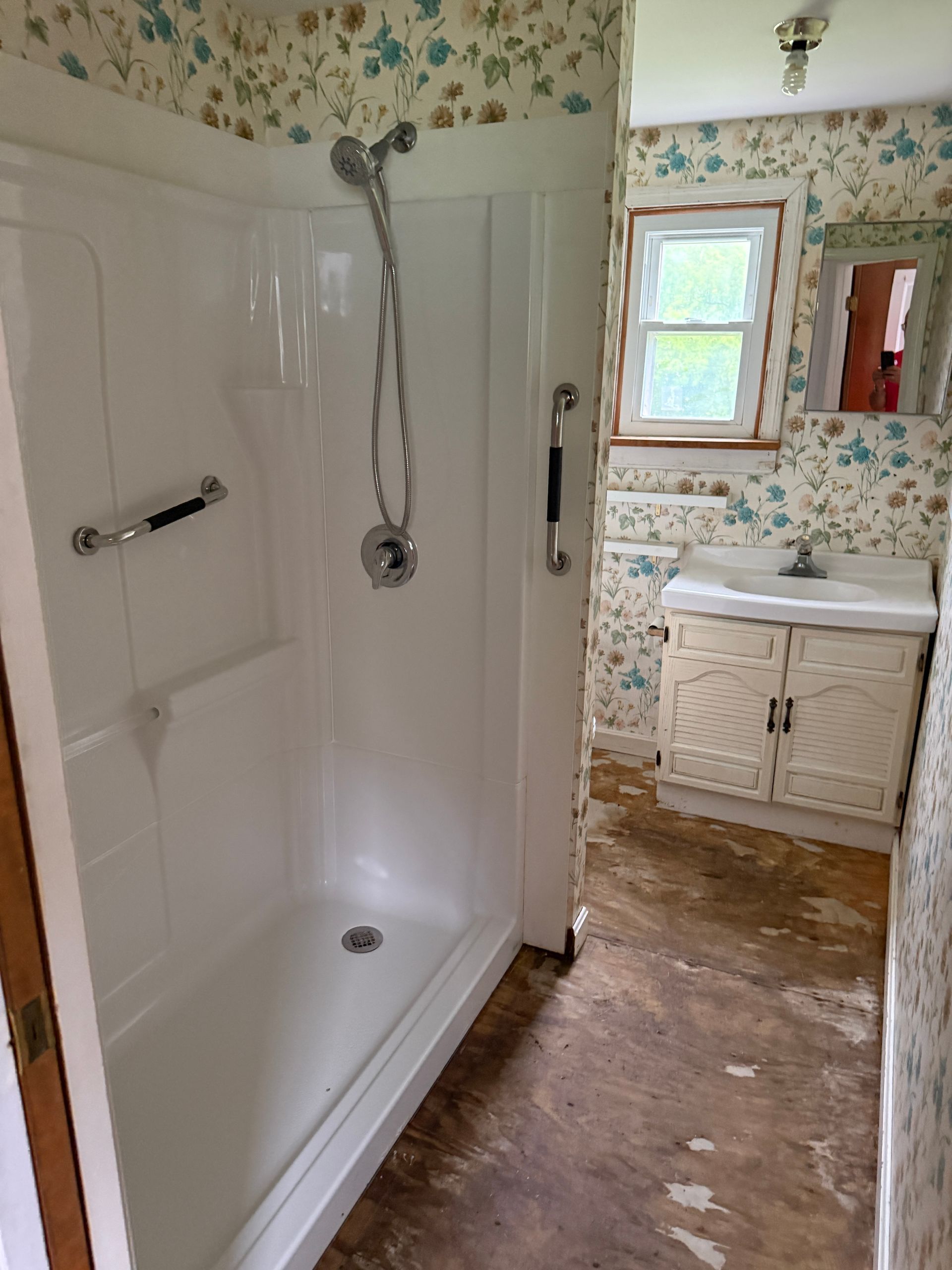 Bathroom with white walk-in shower, floral wallpaper, and a sink vanity in the background.