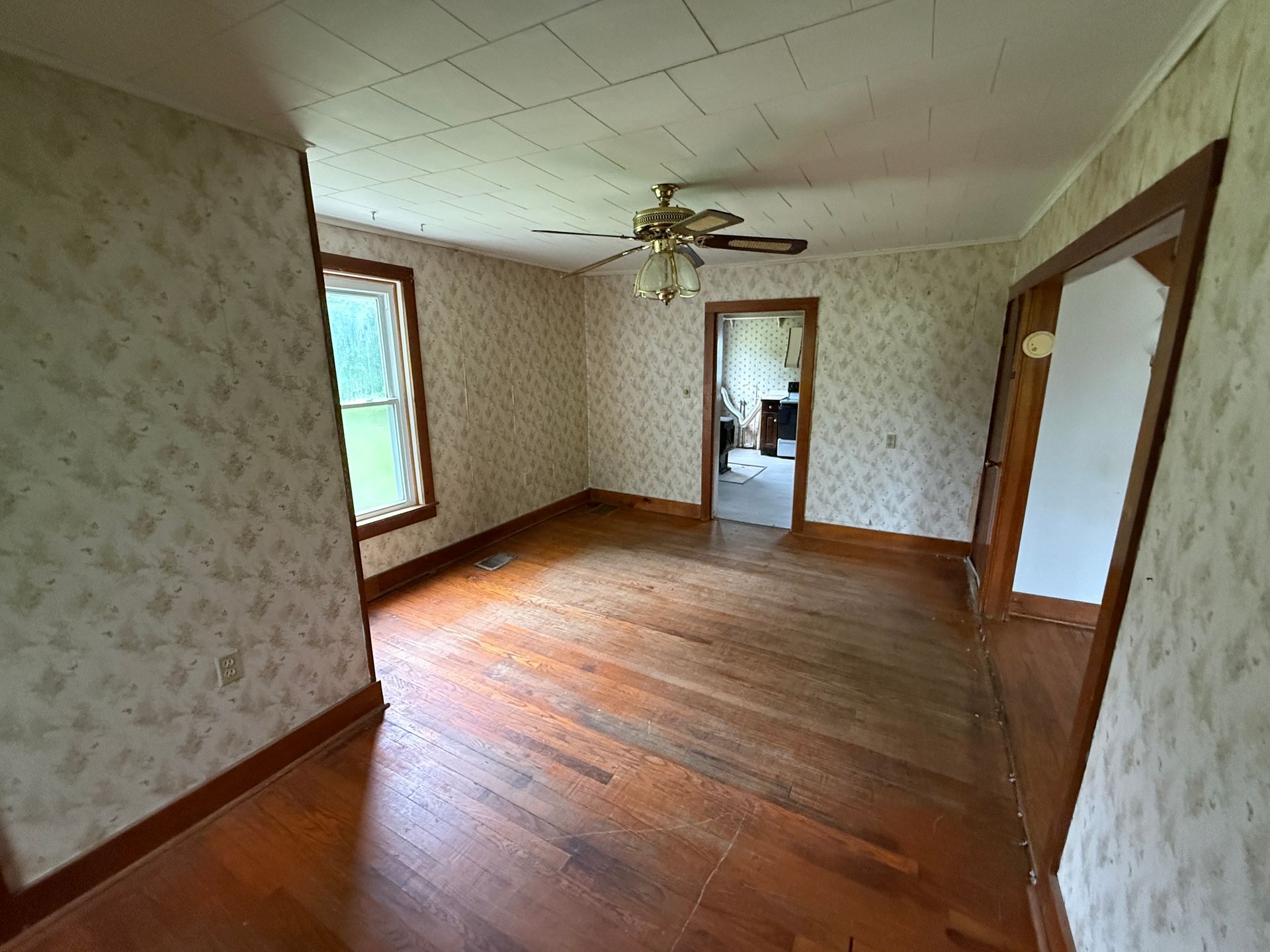 Empty room with wood floors, floral wallpaper, ceiling fan, and windows.