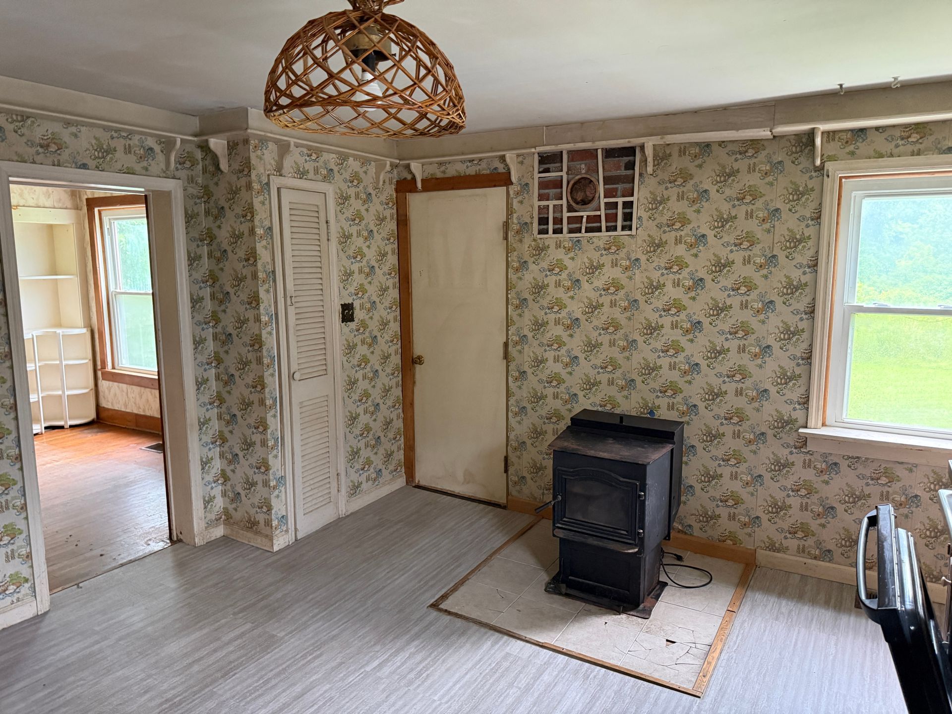Small room with floral wallpaper, wood stove on a rug, and open doorways to adjoining rooms.