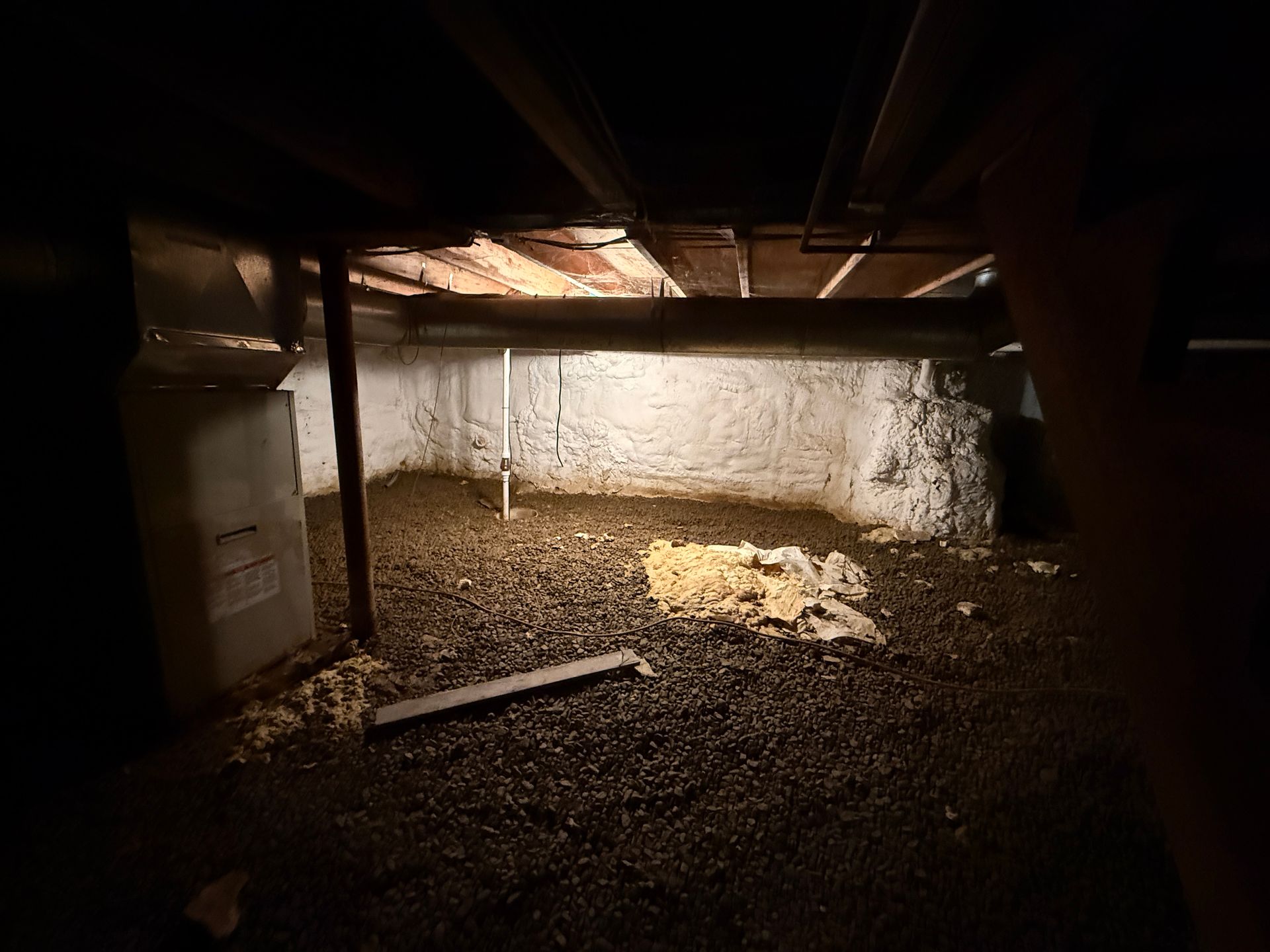 crawl space with a white wall, dirt floor, and a pile of straw under exposed beams.