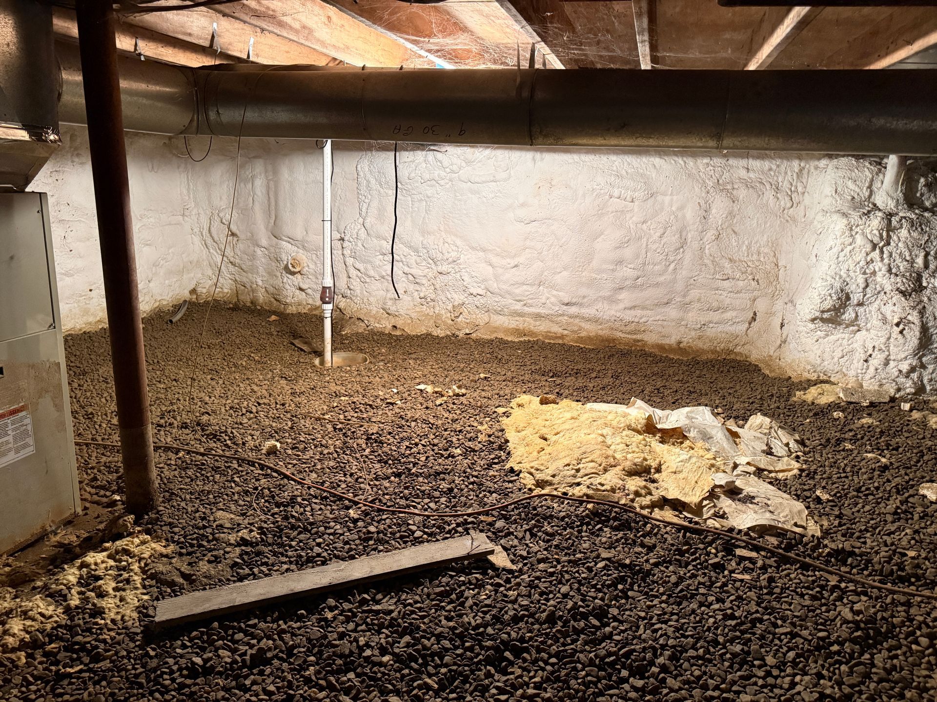 Empty room with dirt floor, and rough white walls under a low wooden ceiling.