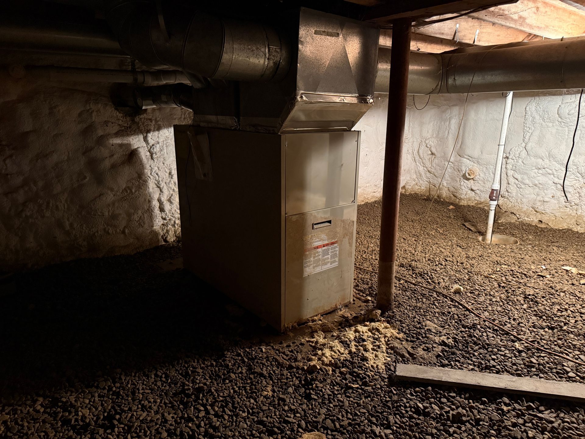 Crawlspace with HVAC ductwork, furnace unit, and gravel floor under a house