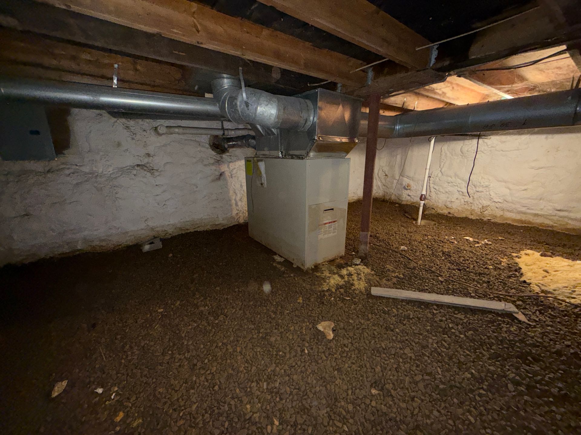 Crawlspace with exposed beams, ductwork, and a white appliance on gravel floor