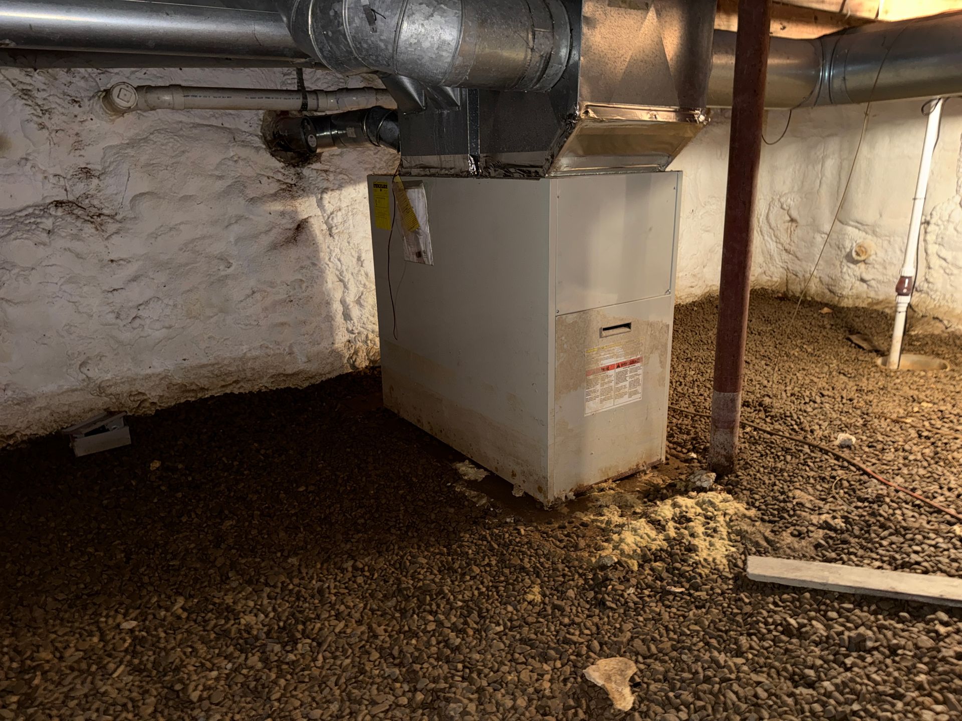 Crawlspace with ductwork and a white furnace under a low ceiling, on a gravel floor.