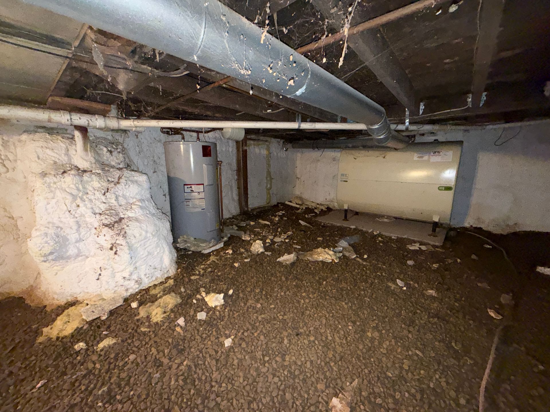 Crawlspace with exposed pipes, white insulation, a water heater, and dirt-covered floor under a house