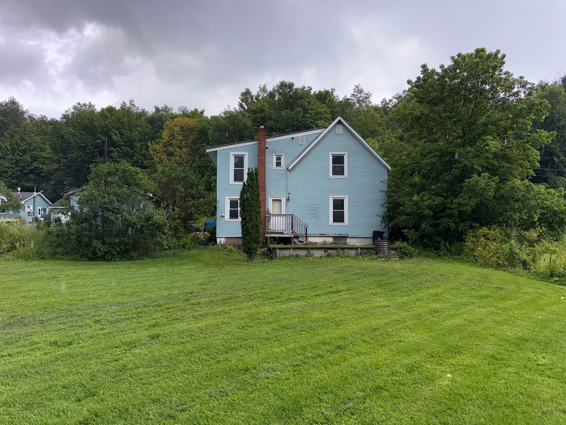Light blue house on a grassy hill with trees and cloudy sky.