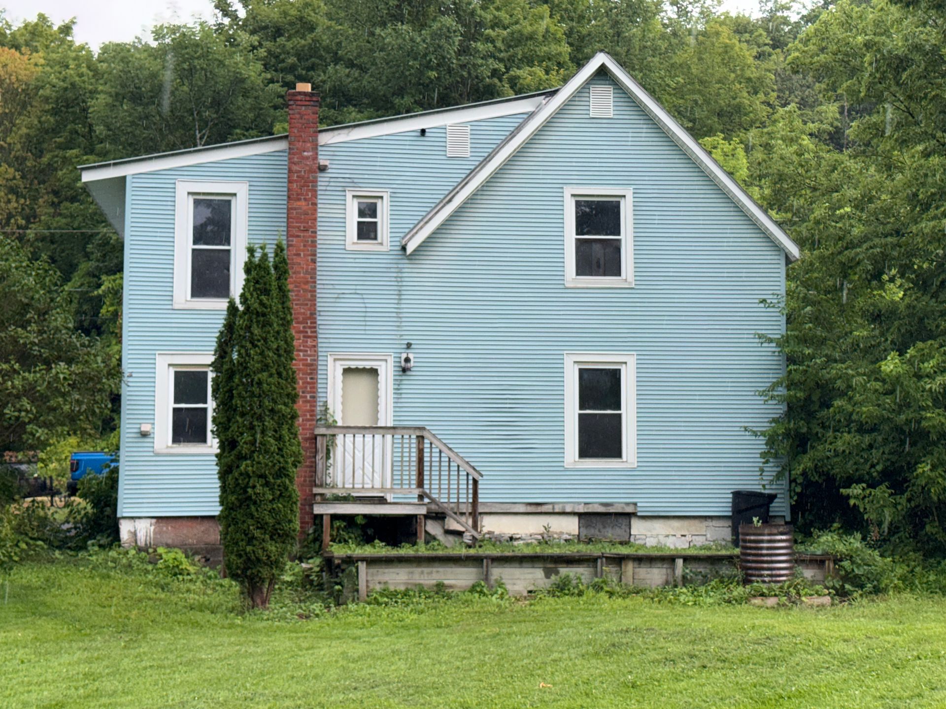 Light blue house with white trim, front porch, and tall brick chimney in a grassy yard.