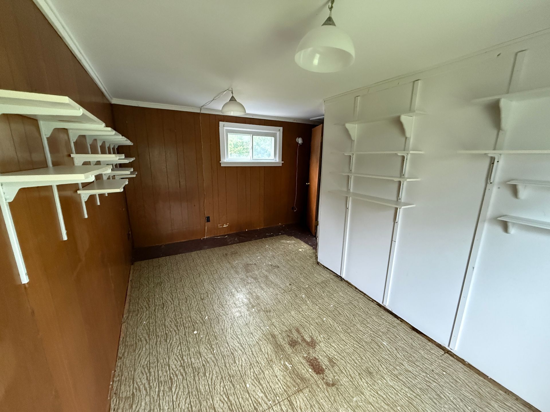 Empty wood-paneled room with built-in white shelves, carpet, and a small window.