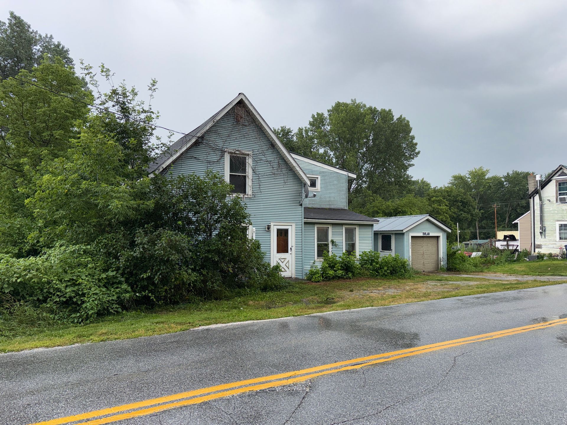 Blue house and garage beside a wet road under cloudy skies
