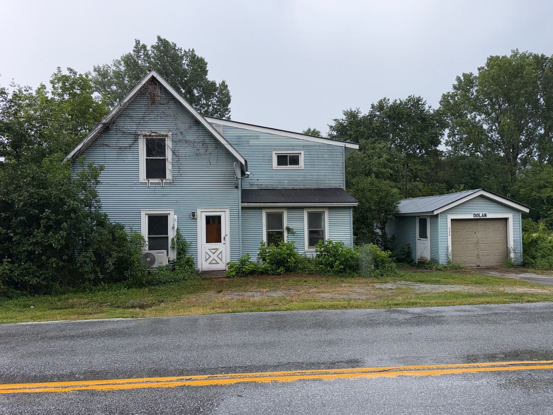 blue house with attached garage beside a road, surrounded by trees.