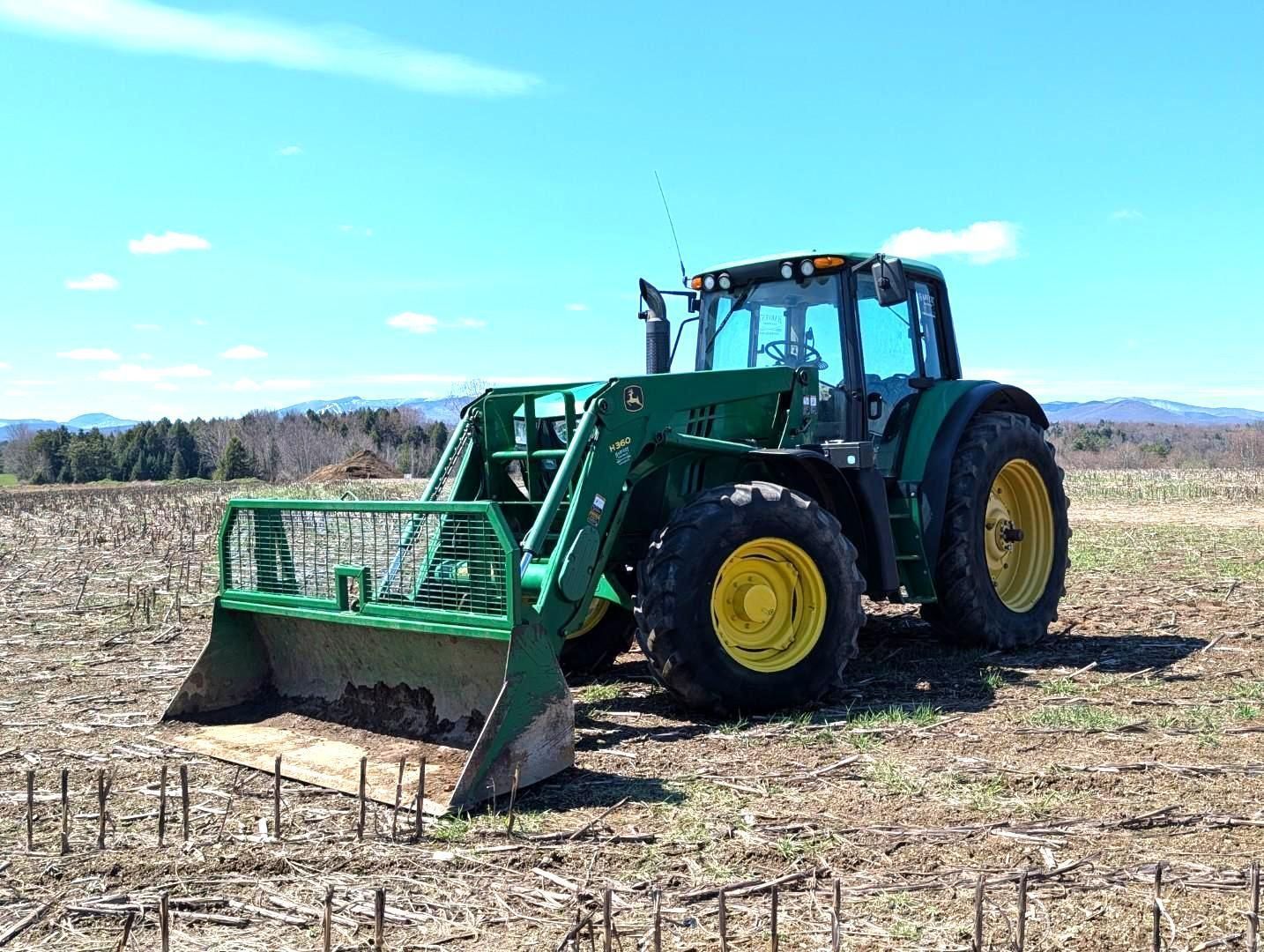 Green tractor with front blade in a field under a blue sky