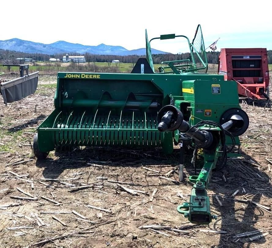 Green John Deere agricultural baler in a field with mountains in the background