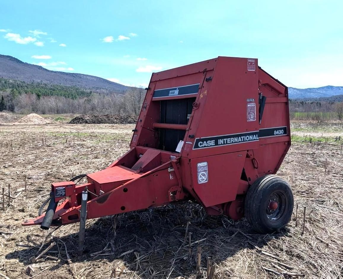Red round baler in a field with mountains in the background