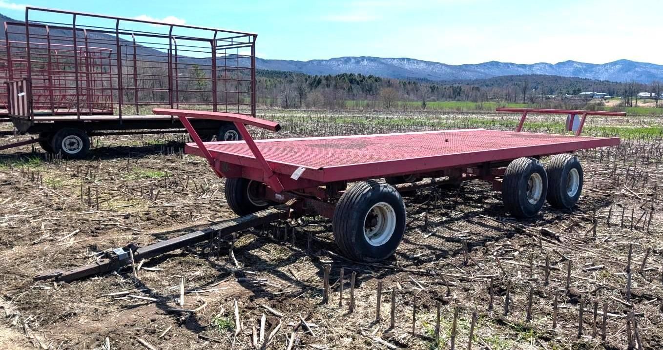 Red flatbed farm trailer in a field with mountains in the background.
