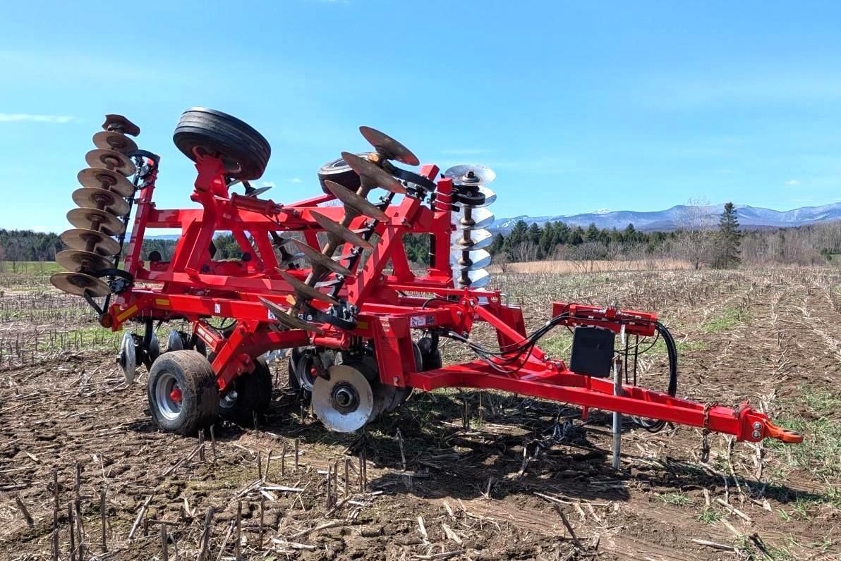 Red farm tillage machine in a field under a clear blue sky