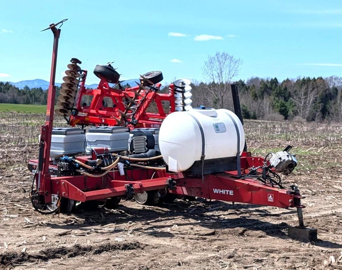 Red farm planter with white tank in a plowed field under a clear sky