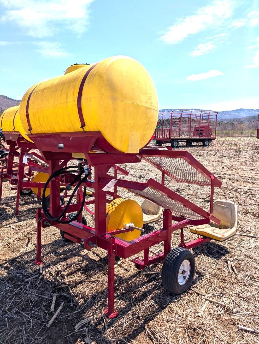 Yellow agricultural tank on a red metal trailer in a field under a blue sky