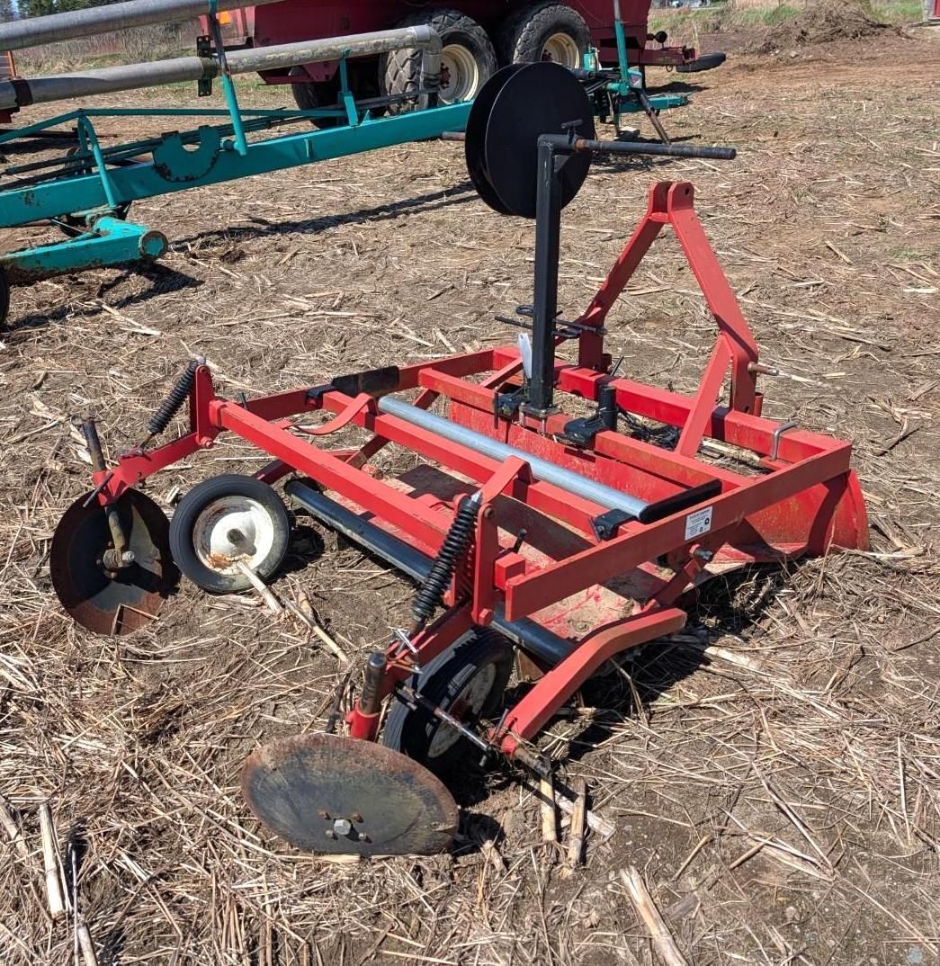 Red farm implement with black disc blades and a central post in a field