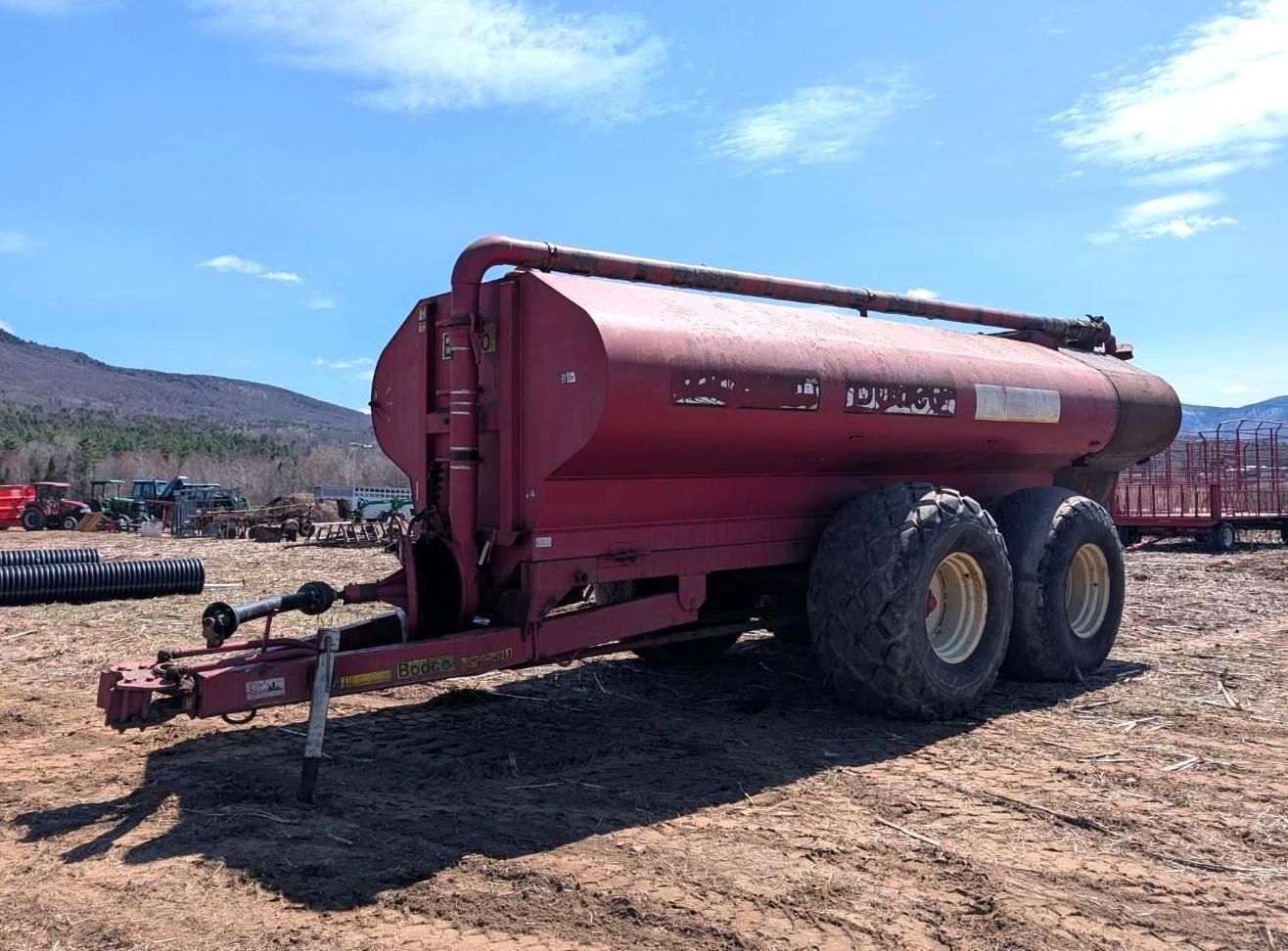 Red livestock trailer with two large tires parked on a dirt lot under a blue sky.