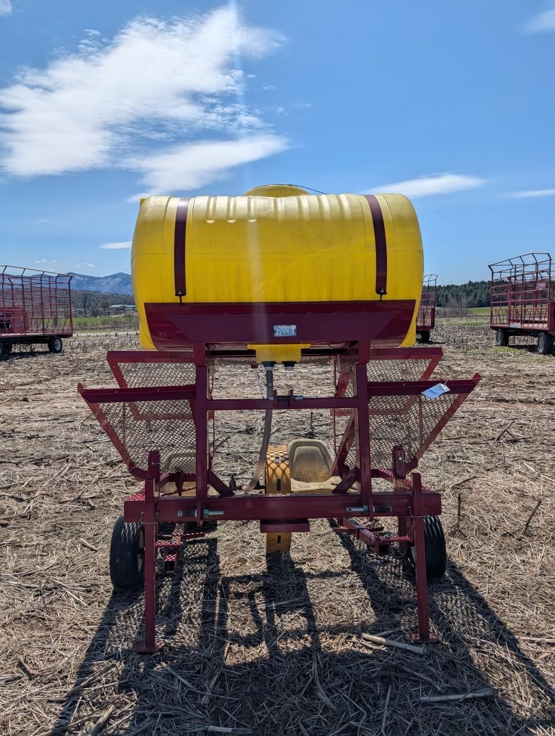 Red farm sprayer with yellow tank in a field under a blue sky