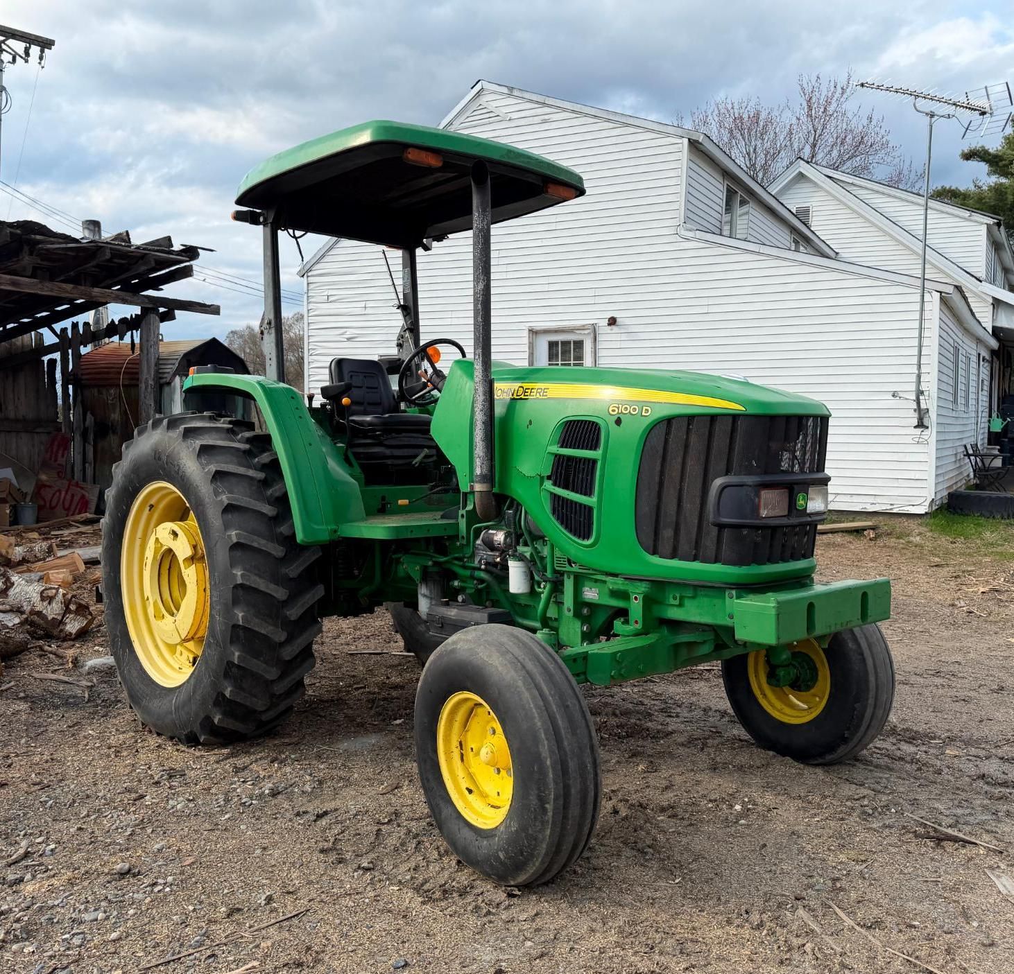 Green tractor with yellow wheels parked on gravel beside a white barn and shed