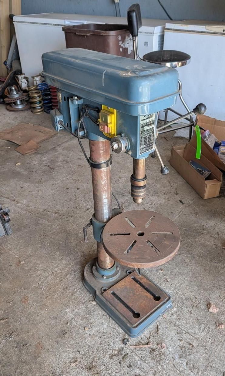 Blue drill press in a workshop, with a round metal table and base.