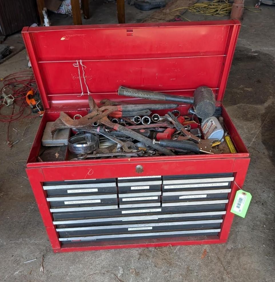 Red metal tool chest with open lid, drawers, and assorted hand tools in a workshop area