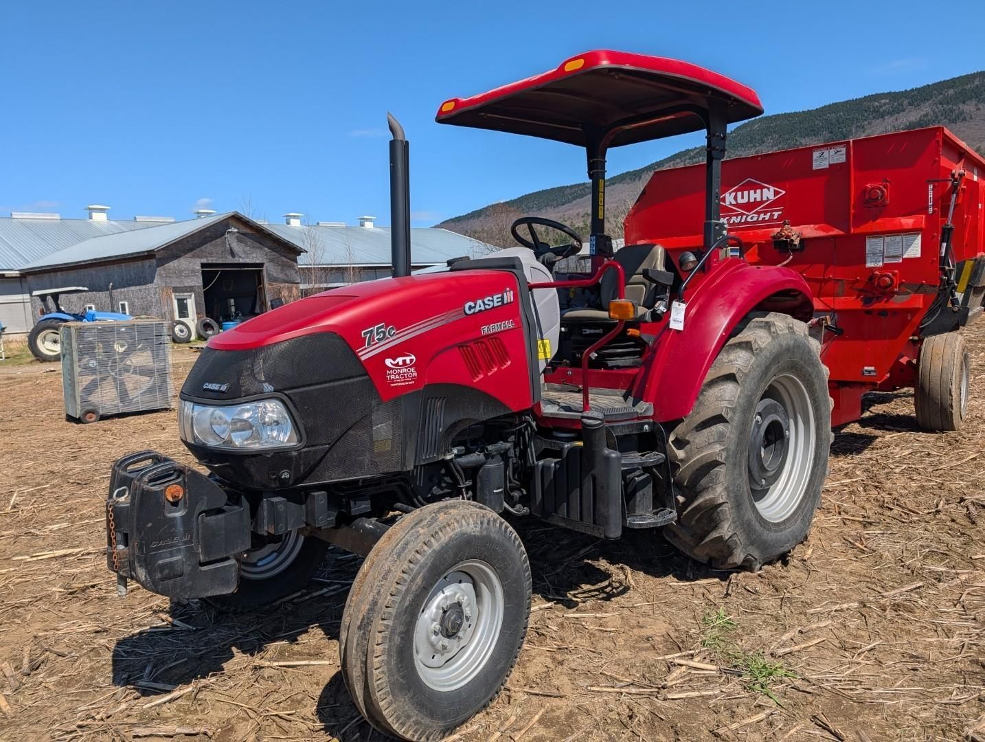 Red tractor with trailer parked on ground under a red canopy at a farm yard
