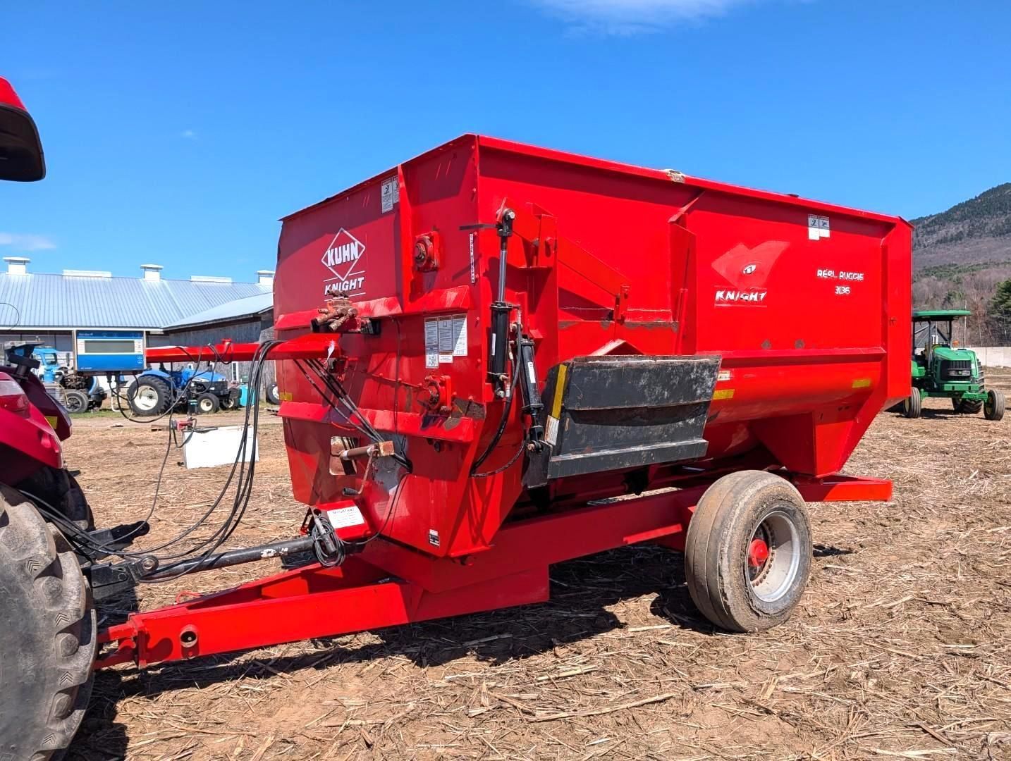 Red grain wagon trailer with a red auger, parked in a dirt lot under a blue sky.