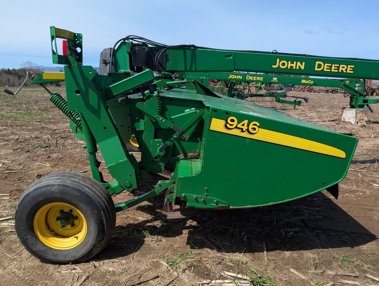 Green John Deere 946 hay baler on a dirt field, side view with yellow wheels.