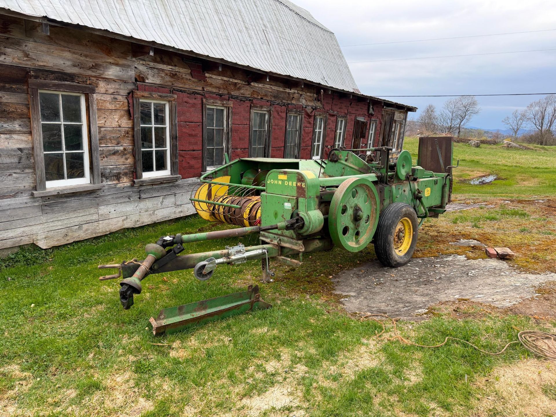Green farm machine parked beside a red barn in a grassy yard.