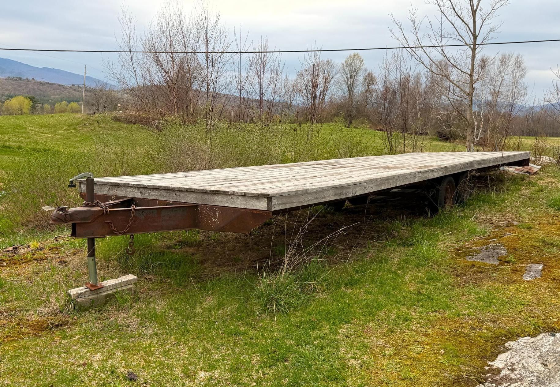 Raised wooden platform on metal supports in a grassy field under an overcast sky