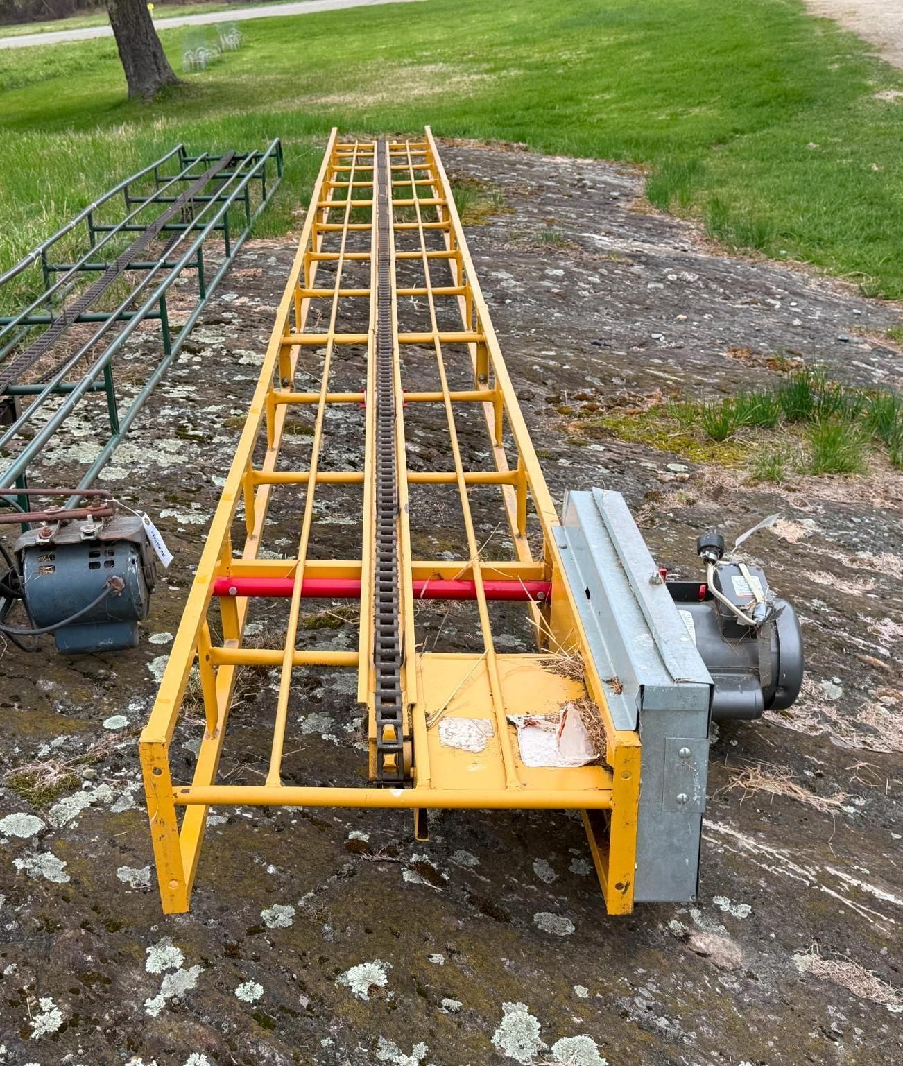 Yellow metal trailer-like equipment with rails and gray machinery, parked on grass and gravel outdoors