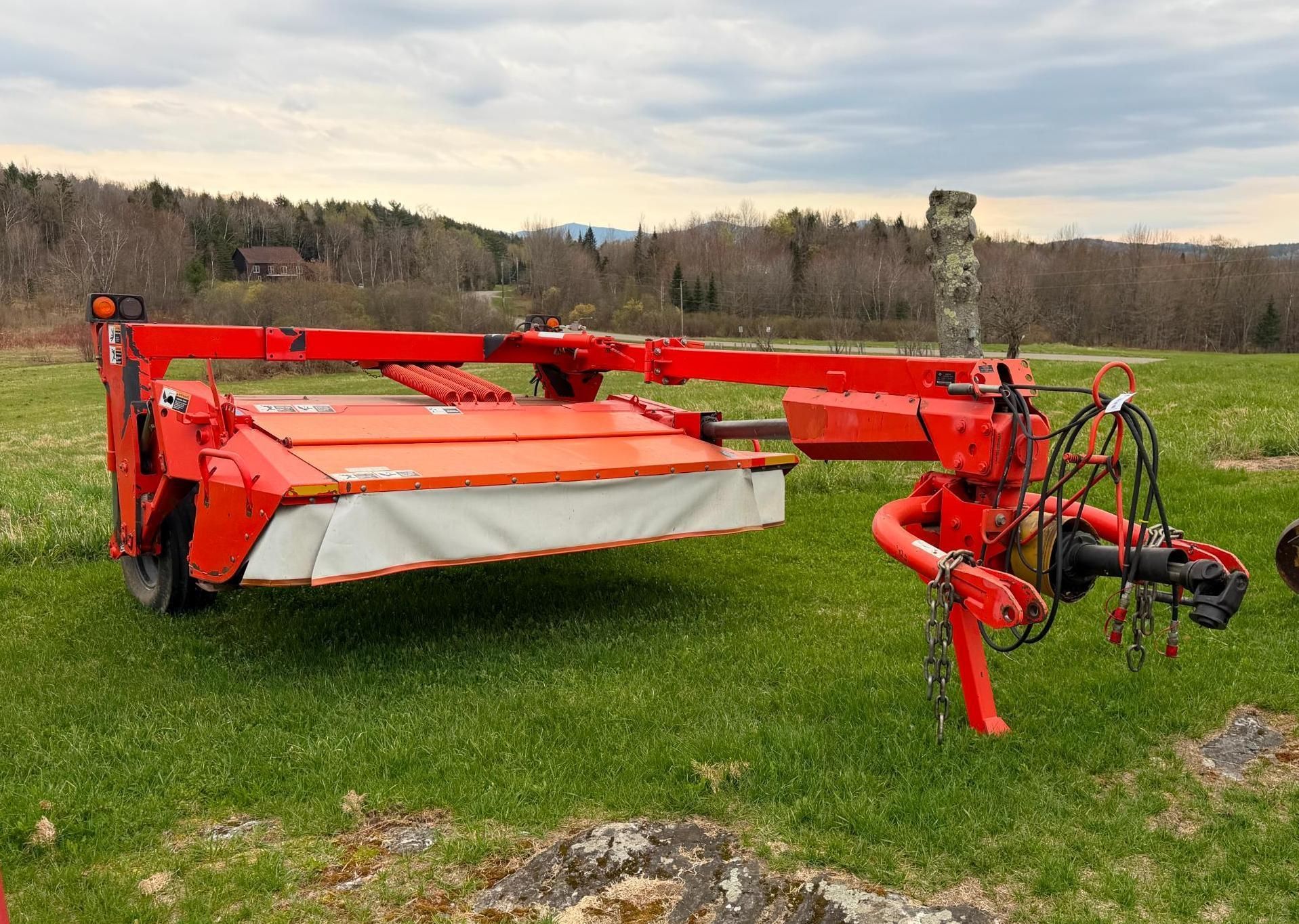 Red agricultural mower on grass field with a white cutting deck and tow hitch