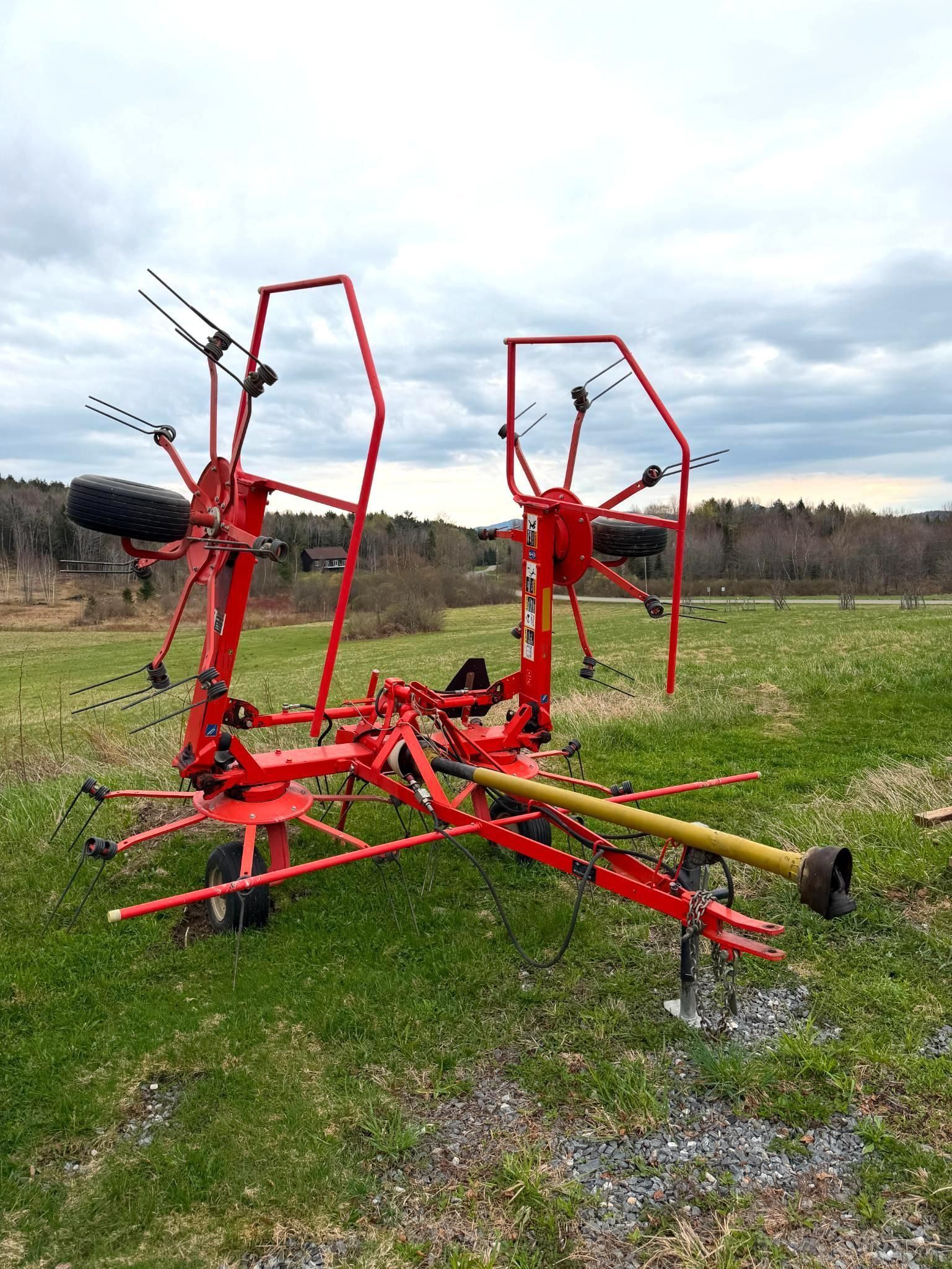 Red farm machinery with tall frames parked in a grassy field under a cloudy sky.