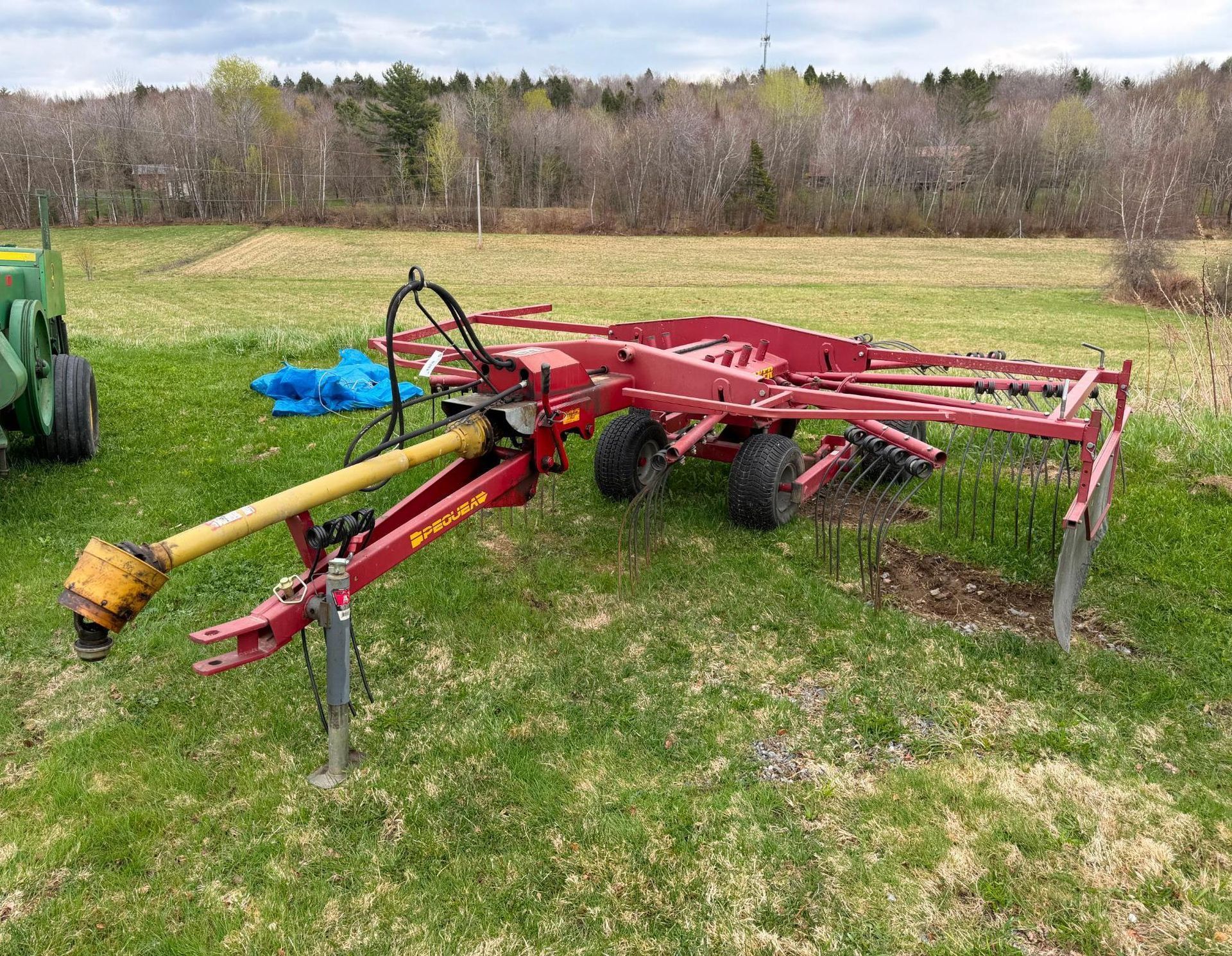 Red farm tillage implement with yellow PTO shaft resting on grass in a field