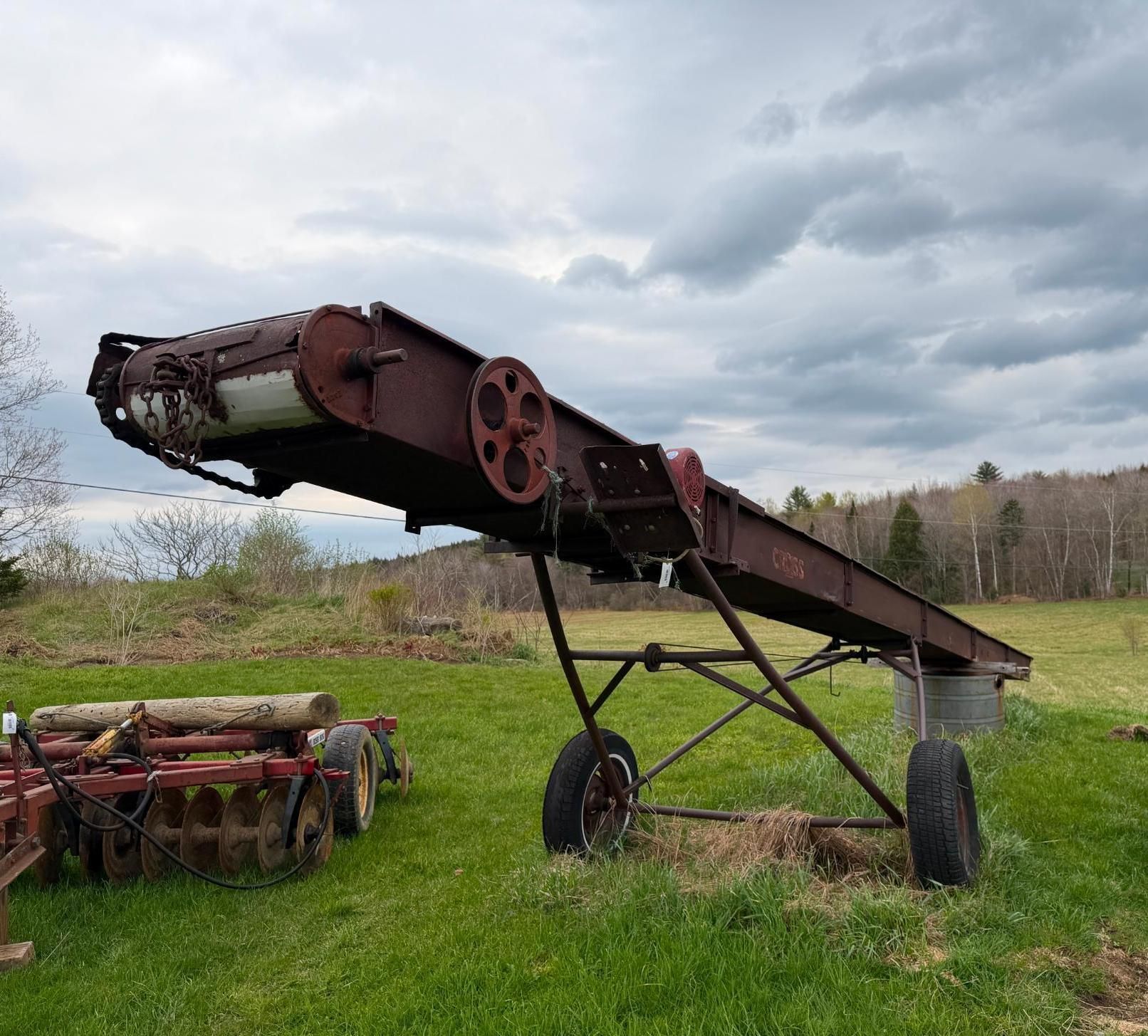 Vintage farm conveyor or harvester on wheels in a grassy field under cloudy sky